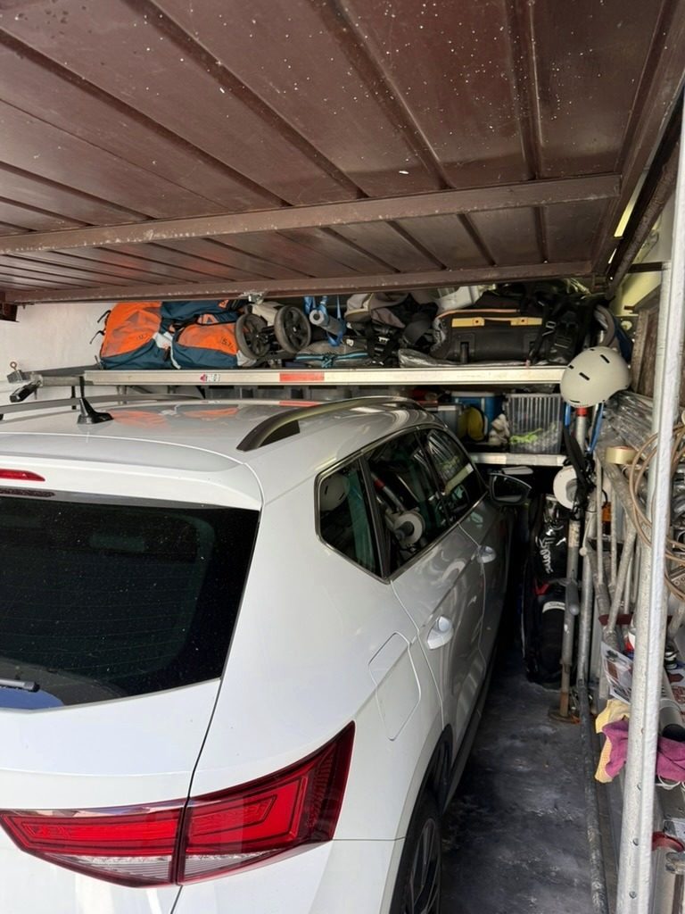 Kombi parkt in einer Garage, direkt über dem Dach liegt eine Ablage-Ebene aus Layher-Gerüstböden mit Reisetaschen, Kinderwagen und Ausrüstung