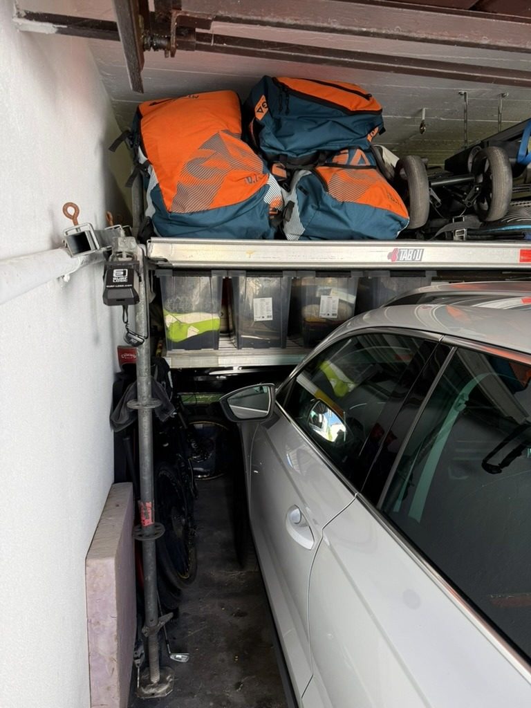 Allround-Stiel an der Garagenwand mit Fußspindel, darüber zwei Ebenen mit Sortierkisten und Taschen