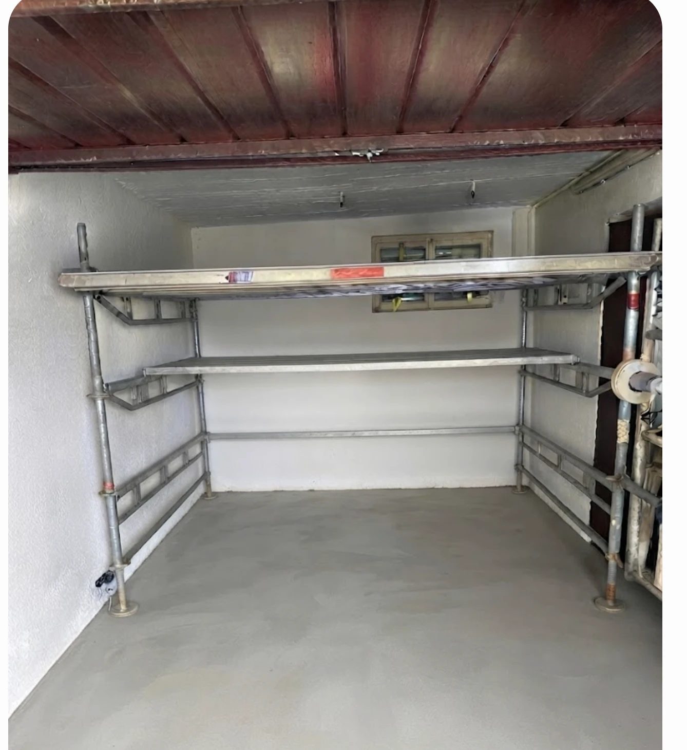 Das Gestell in der leergeräumten Garage: zwei Ablage-Ebenen an den Seitenwänden, Stiele auf Fußspindeln, der Stellplatz in der Mitte bleibt frei